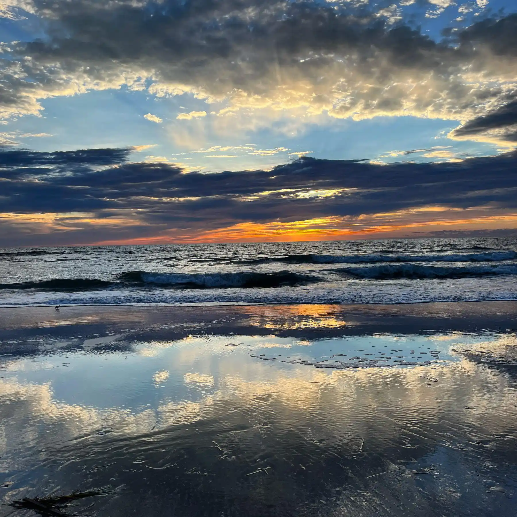 Sunrise over the ocean at St Simons Island, clouds reflected on wet sand